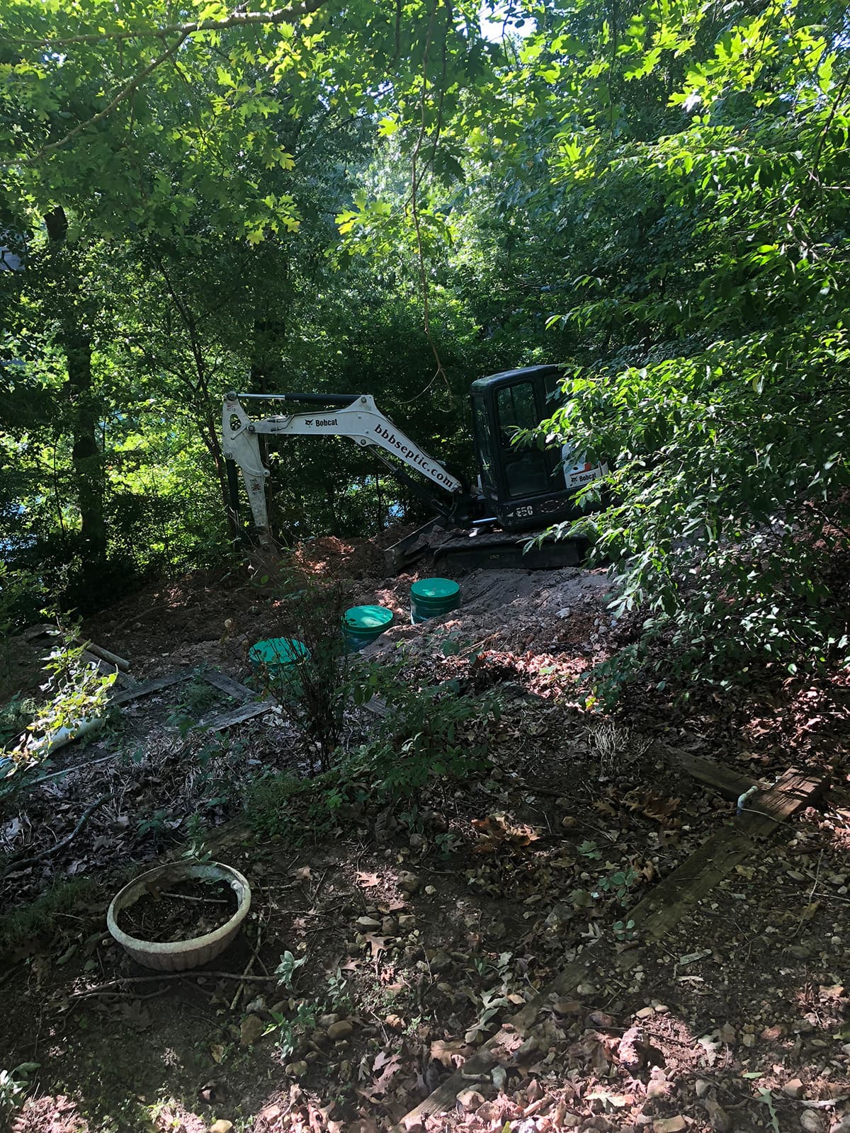 BBB excavator setting risers on a wooded septic install site